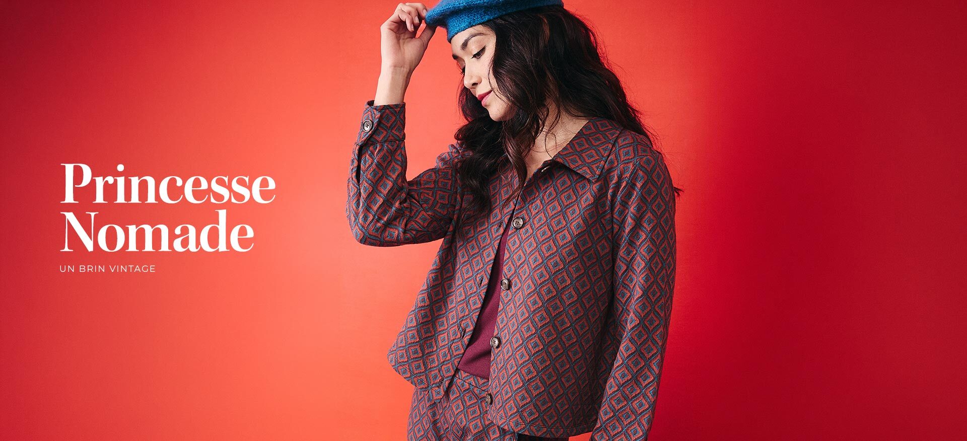 mannequin-portant-un-ensemble-veste-et-pantalon-a-motif-geometrique-rouge-et-bleu-avec-un-beret-bleu-sur-fond-degrade-rouge-orange--princesse-nomade-