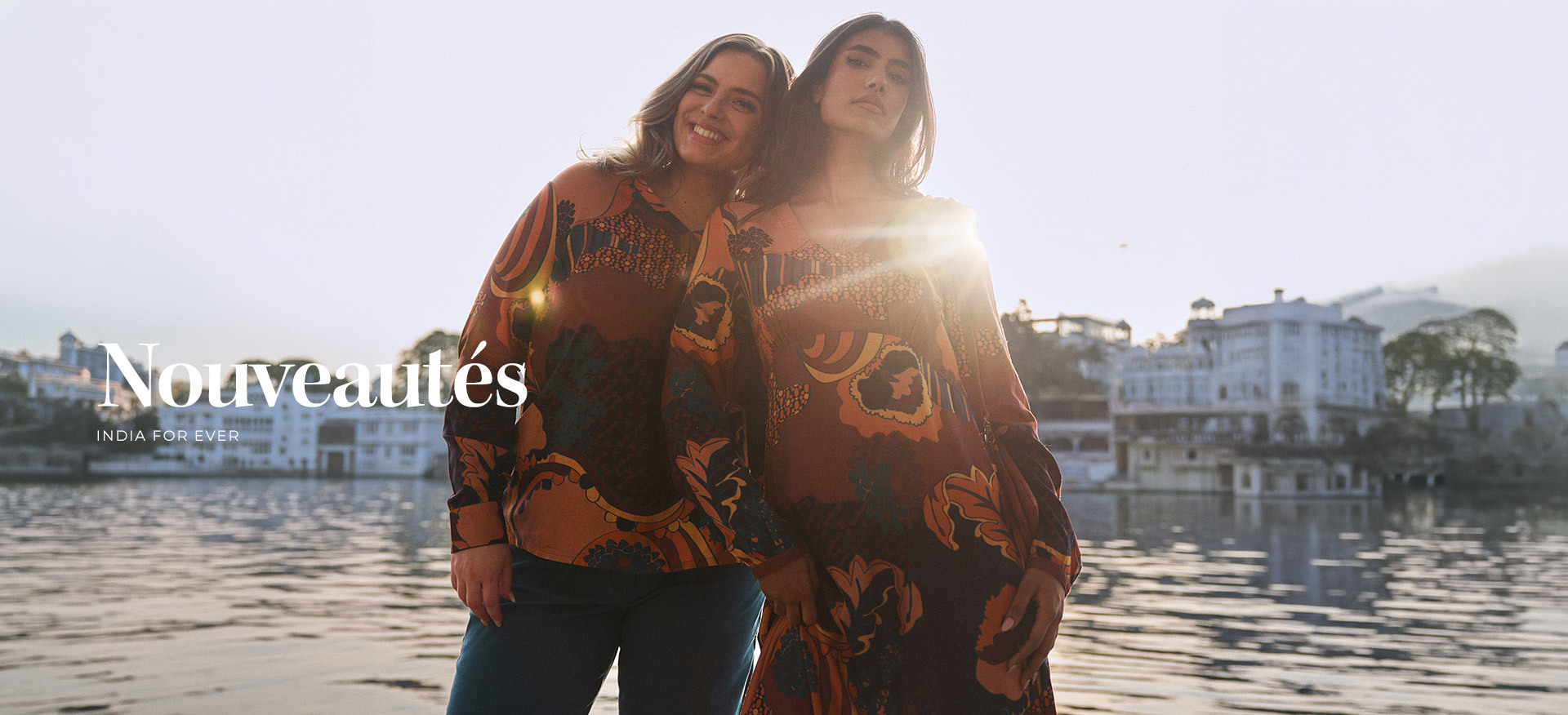 deux-femmes-posant-au-bord-de-l-eau-au-coucher-du-soleil-portant-des-vetements-de-la-collection--nouveautes---india-for-ever--aux-motifs-imprimes-dans-les-tons-marron-orange-et-ocre-